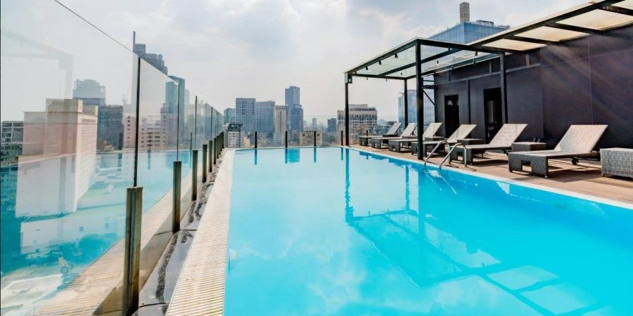 The hotel pool is enclosed by transparent glass walls, creating a bright and airy atmosphere.